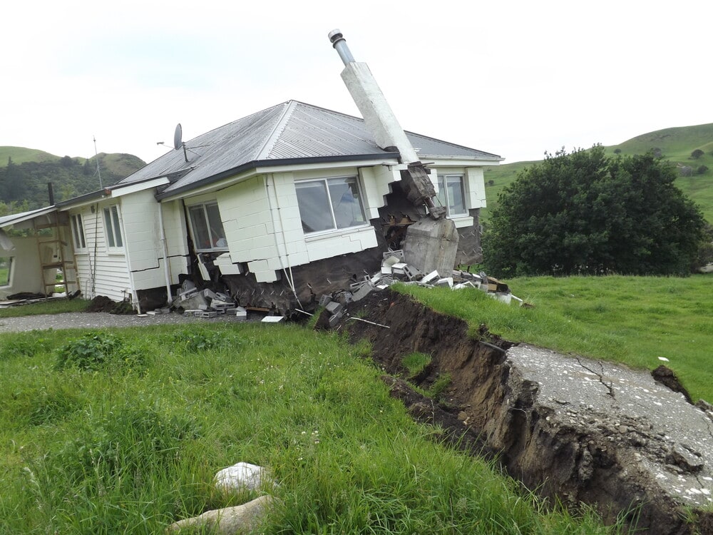Grassy land ripped open in front of a badly damaged home from the Kaikōura Earthquake of 2016. The chimney is at an odd angle, and the land deformation has happened right beneath this unlucky home.